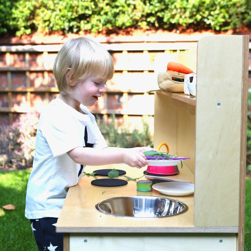 happy toddler plating with the mud kitchen close up