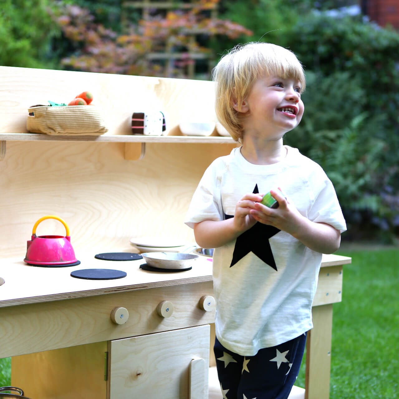 happy toddler playing with the mud kitchen in the garden