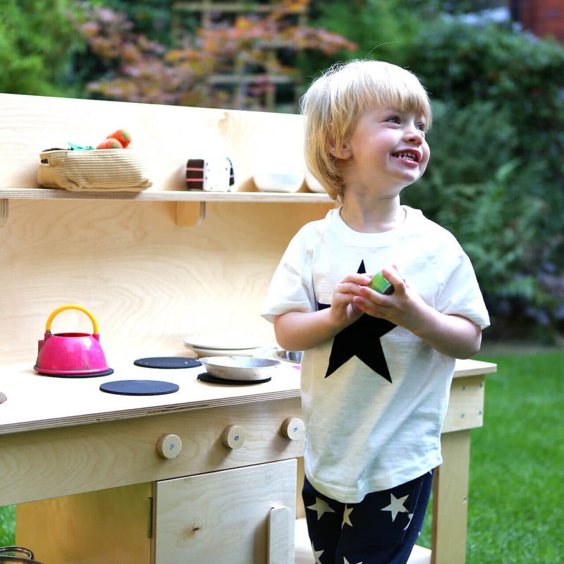happy toddler playing with the mud kitchen in the garden